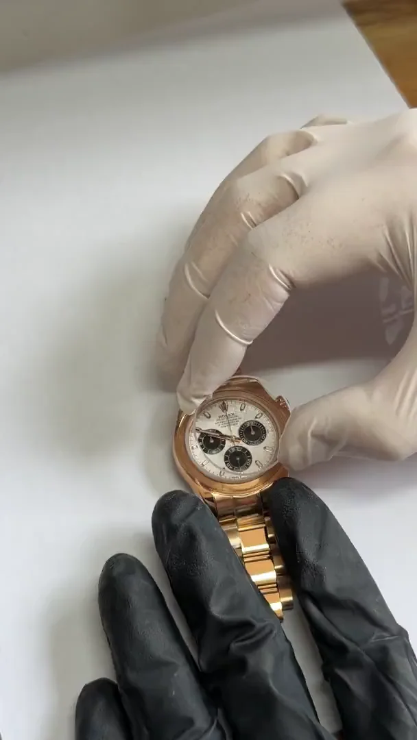 Gloved hands handling a rose-gold-tone chronograph with a light dial at the workshop bench