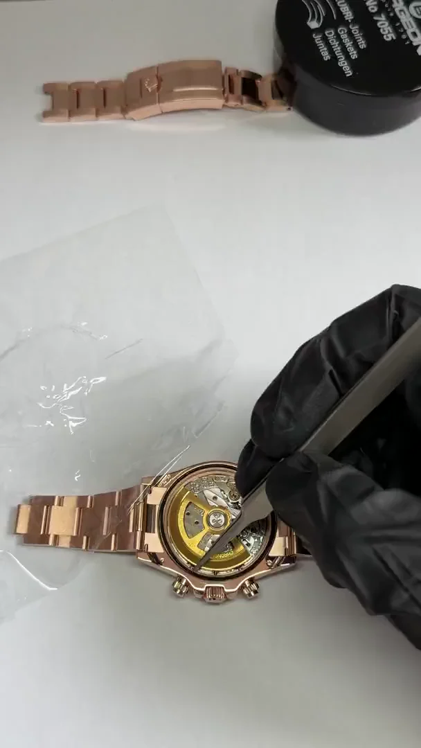 A gloved hand working beside the exposed movement of a rose-gold-tone chronograph